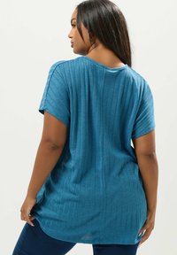 Turkoosinvihreä kapealinjainen paita lyhyillä hihoilla, pyöreällä kaula-aukolla ja kevyellä kankaalla; siinä on pystysuorat raidat tekstuurin luomiseksi sekä rento istuvuus.