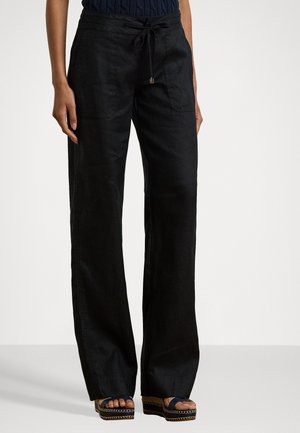 Vrouw draagt losse zwarte linnen broek met voorzakken en een trekkoortje in de taille, gecombineerd met donkere platformsandalen.