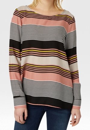 Femme portant un haut à manches longues avec des rayures horizontales roses, noires, blanches et jaunes, assorti d’un jean bleu foncé.