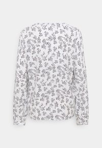 Blusa a manica lunga comoda di colore bianco con un motivo floreale nero. Tessuto morbido, scollo rotondo e polsini leggermente arricciati.