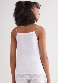 Witte mouwloze top van lichte stof met delicate kantafwerking aan de onderkant. Verstelbare spaghettibandjes, losse pasvorm, minimale textuur.