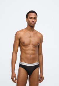 Μαύρα βαμβακερά σλιπ με ζώνη μέσης με το ασημένιο λογότυπο Tommy Hilfiger, εφαρμοστή σχεδίαση, λεία υφή και ελάχιστη κάλυψη.