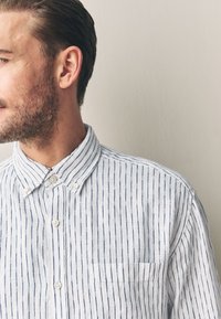 Hellblaues Hemd mit Kragen und weißen vertikalen Streifen. Mit einer Tasche auf der linken Brustseite und strukturierter Stoff.