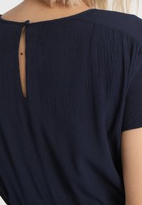 Haut bleu marine à manches courtes, en tissu texturé, avec une ouverture en forme de clé à l'arrière et un col rond.