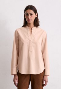 Camicia a maniche lunghe rosa chiaro con scollo a V e orlo dritto, realizzata in tessuto morbido, con un design minimalista e dettaglio con bottone al colletto.
