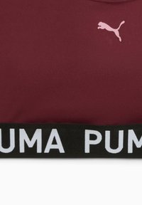 Bordo sportski gornji dio od mekane tkanine koji ima mali ružičasti Puma logo i crnu elastičnu traku s natpisom "PUMA" u podebljanim bijelim slovima.