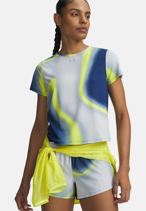 Vrouw met gevlochten haar die een blauw, geel en wit sportshirt met korte mouwen draagt en bijpassende shorts met een geel jasje om haar taille gestrikt.