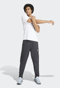 Weißes Sport-T-Shirt kombiniert mit schwarzen Hosen, beide aus leichtem Material. Verfügt über einen elastischen Bund und dezente Branding-Elemente an den Hosen.