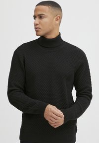 Maglione a collo alto nero con un motivo a trama a nido d'ape, polsini e orlo a coste. Presenta una silhouette aderente e moderna.