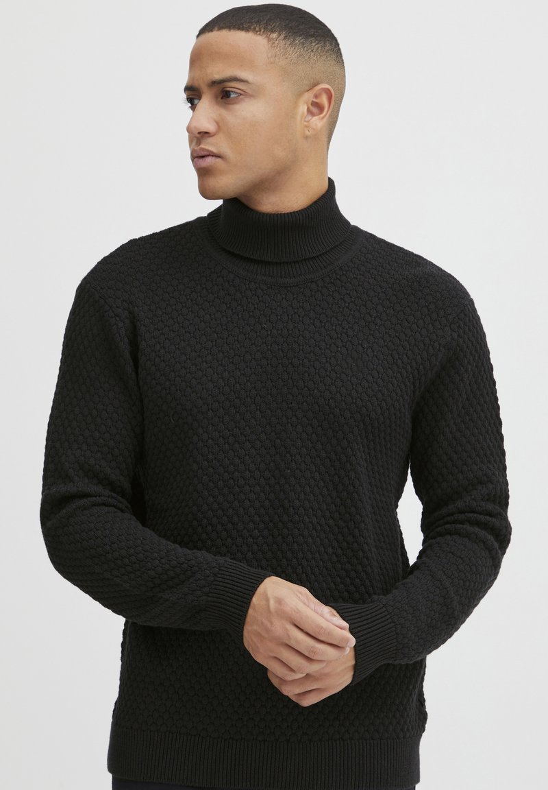 Maglione a collo alto nero con un motivo a trama a nido d'ape, polsini e orlo a coste. Presenta una silhouette aderente e moderna.