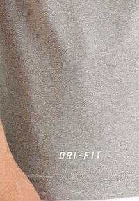 Grå DRI-FIT atletisk t-shirt tyg, slät textur, kortärmad design och centrerad logo på fållen i vitt, vilket framhäver andningsförmågan.