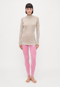 Beige langermet topp med teksturert mønster og kvart glidelås, kombinert med rosa leggings med diamantmønster og sidestriper.