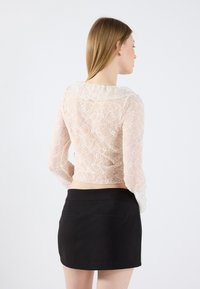 Lace langermet topp med volangkrage i lys rosa, kombinert med et svart, tettsittende miniskjørt med to baklommer.