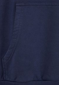 Gros plan d'une poche en tissu bleu marine avec des coutures visibles et un ourlet côtelé, probablement partie d'un sweat-shirt ou d'un hoodie.