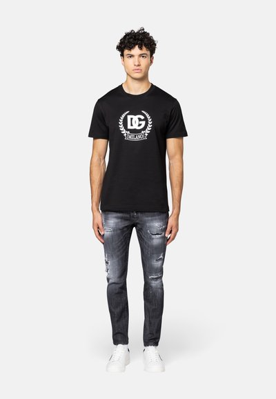 Zwarte katoenen t-shirt met een wit logo en lauriert ontwerp op de voorkant, gecombineerd met versleten grijze jeans en witte sneakers.