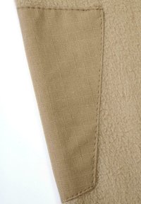 Beigefarbene Textildetails mit zwei verschiedenen Texturen: eine weiche, pelzige Oberfläche und ein glattes, kariertes Gewebe mit sichtbaren Nähten.