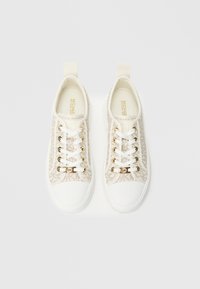 Λευκά πάνινα αθλητικά παπούτσια με χρυσές λεπτομέρειες, με επάνω μέρος από υφασμάτινο σχέδιο, λευκή καουτσούκ σόλα και κλασικό κορδόνι.