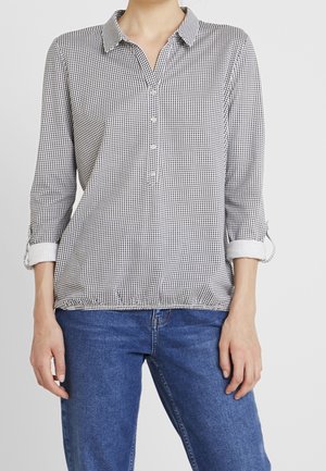Blusa a scacchi bianco e nero con colletto, apertura frontale con bottoni e maniche a tre quarti. Il tessuto è morbido con orlo elastico.