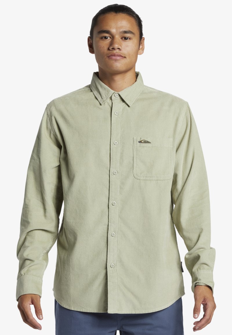 Lichtgroene corduroy blouse met lange mouwen, knoopsluiting en borstzak. Heeft een logo op de zak. Zachte textuur en ribbelontwerp.