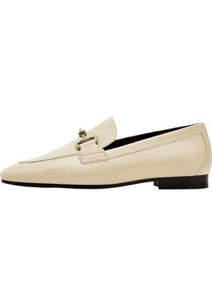 Mocassins en cuir beige avec un design à bout pointu, présentant un détail en boucle métallique décorative et un petit talon noir. Texture lisse.