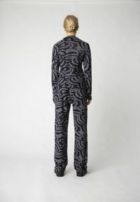 Schwarzes gemustertes Loungewear-Set mit einem Langarmoberteil und weit geschnittenen Hosen mit texturierten, wirbelnden Designs. Glatter Stoff mit einer taillierten Silhouette.