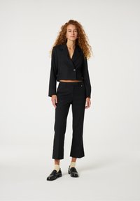 Zwarte cropped blazer met één knoop, gecombineerd met op maat gemaakte zwarte broek met een lichte flaring en zwarte loafers met details.