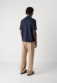 Polo shirt blu navy con finitura texture, maniche corte e colletto piatto, abbinato a pantaloni beige a gamba larga e scarpe nere.