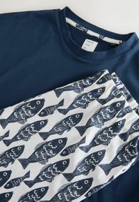 Tricou bleu marin asortat cu pantaloni albi cu un model repetitiv de pești întunecați și talie elastică.