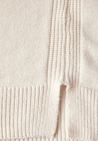 Pullover morbido di colore crema con texture a coste, caratterizzato da strisce verticali e orizzontali e un piccolo dettaglio di spacco laterale.