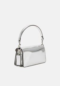 Borsa metallizzata argento con forma rettangolare, texture liscia, manico corto e targhetta decorativa attaccata.