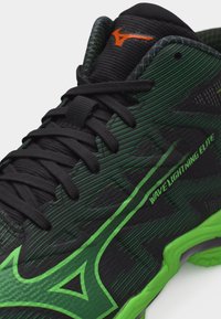 Μαύρο και πράσινο αθλητικό παπούτσι με μαύρα κορδόνια, πορτοκαλί λογότυπο στη γλώσσα και το κείμενο «Wave Lightning Elite» στο πλάι.