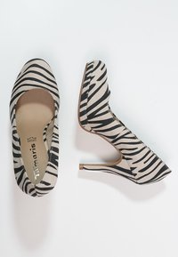 Beige high-heeled shoes with black zebra stripes, made of fabric, featuring a rounded toe and a pointed heel design.