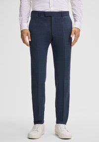 Pantaloni sartoriali blu navy con un leggero motivo testurizzato, fondo piatto, tasche laterali e cintura, abbinati a sneakers bianche.