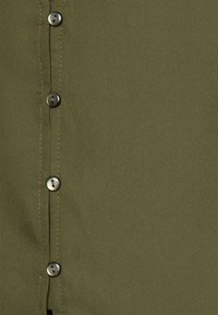 Camicia verde oliva con bottoni, caratterizzata da una texture del tessuto liscia, sei bottoni metallici e dettagli cuciti lungo la patta dei bottoni.