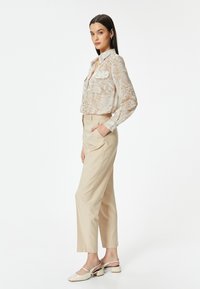 Beige linnen broek met zijzakken, gecombineerd met een licht, geblokt blouse met een kraag. Schoeisel: crèmekleurige slingback hakken met een blokhak.