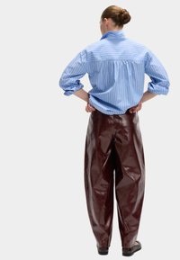 Niebieska i biała w paski koszula z guzikami, luźny krój, połączona z błyszczącymi, ciemnoczerwonymi spodniami o szerokich nogawkach, prezentującymi gładką teksturę.