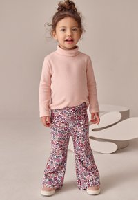 Ljusrosa polotröja kombinerad med blommönstrade utsvängda byxor i röda, rosa och blå toner. Skor är beigea tofflor.