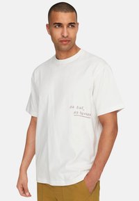 Weißes T-Shirt aus Baumwolle mit kurzen Ärmeln und rundem Ausschnitt. Text "Kein Risiko, keine Belohnung" in Pink auf der linken Brustseite.