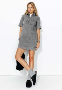 Robe en denim gris à manches courtes, avec deux poches poitrine et des détails cousus. Associée à des sabots noirs et des chaussettes grises. Coupe simple et décontractée.