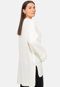 Maglione bianco lavorato a maglia con una vestibilità rilassata, caratterizzato da spacchi laterali e polsini a costine, abbinato a leggings neri per un contrasto.