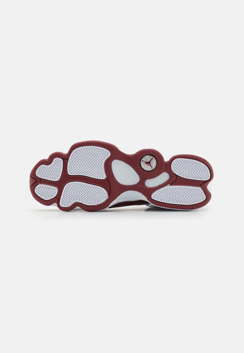 Semelle de sneaker blanche et bordeaux avec un motif de crampons en chevron et un évidement circulaire visible comportant un logo Jumpman rouge près de l'arche.