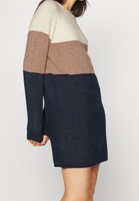 Abito in maglia con maniche lunghe, caratterizzato da righe orizzontali nei colori panna, marrone e blu navy, che mette in risalto una texture morbida e una silhouette rilassata.
