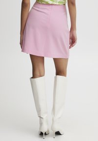 Roze mini-jurk met een rechte snit, gladde stof en een detail met rugnaad. Gedragen met hoge witte, geribbelde, haklaarzen.