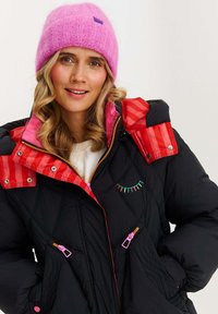 Čierna vatovaná bunda s červenými a ružovými akcentmi, s kapucňou, pruhovanými detailmi a farebnou výšivkou. Ružová pletená čiapka.
