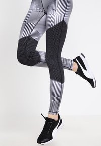 Sort-og-hvidmønstrede leggings med geometriske designs, teksturerede sorte paneler og matchende sorte sportsko.