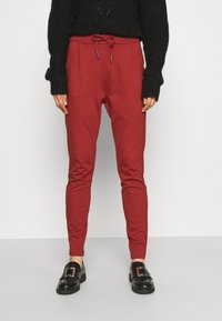Röda tapered byxor med elastisk dragsko i midjan, som har sidofållar och en mjuk bomullstextur, kombinerade med svarta loafers.