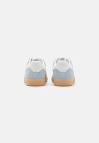Sneaker blu in suede con accenti bianchi, caratterizzati da un profilo basso e una suola in gomma naturale, cuciture visibili e una finitura testurizzata.
