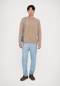 Beige vlněný svetr, světle modré pruhované kalhoty a hnědé boty. Malá modrá kabelka přes rameno. Jednoduchý design a uvolněný střih.