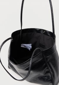 Sac à épaule en cuir noir avec le haut ouvert montrant une doublure en tissu noir et une étiquette d'entretien visible à l'intérieur.