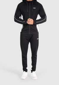 Sudadera con cremallera de athletic negra y pantalones con franjas blancas, hecha de tejido suave, que cuenta con capucha ajustable y detalle de logo.